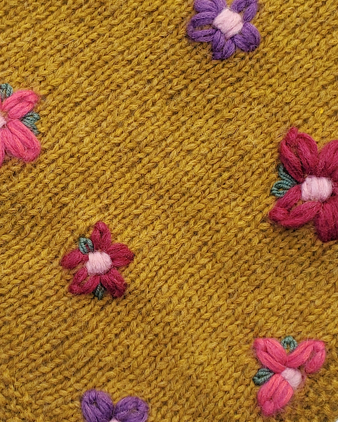 Detailansicht mehrerer Stickblumen auf senfgelben Strick