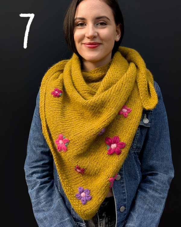 Modell trägt senffarbenes Stricktuch, bestickt mit violetten Blüten
