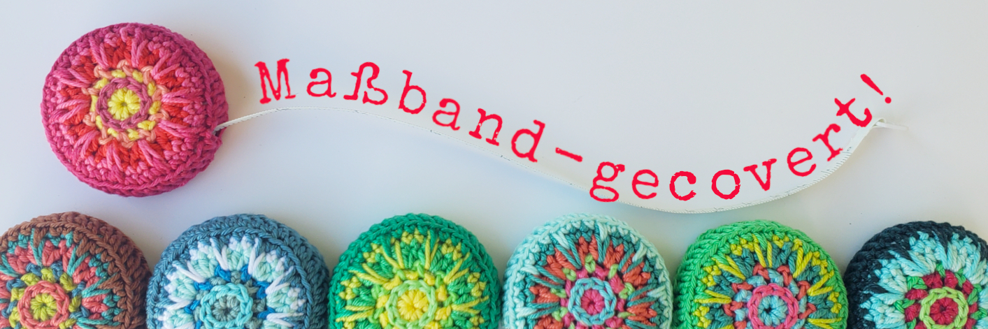 Aufsicht auf mehrere bunte umhäkelte Maßbänder, Schriftzug Maßband - gecovert!