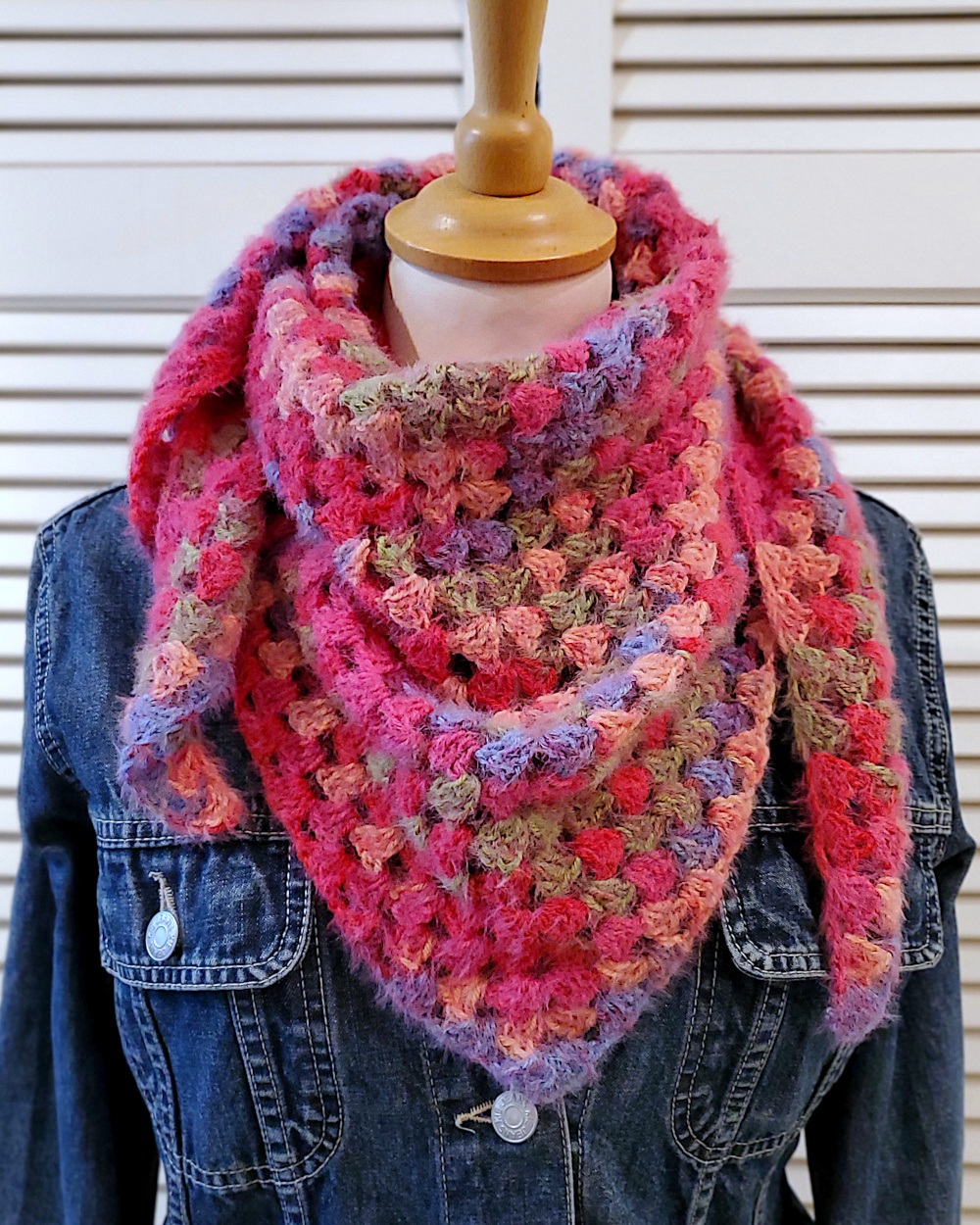 Schneiderpuppe mit rot-pink-blauem Häkeltuch auf Jeansjacke drapiert